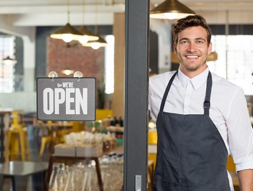 Smiling café owner in doorway with open sign